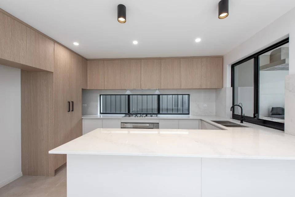 Modern kitchen with minimalist design, featuring a sleek island, light wood cabinets, and stainless steel appliances.