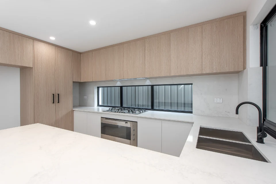 Modern kitchen with light wood cabinets, marble countertop, and stainless steel appliances.