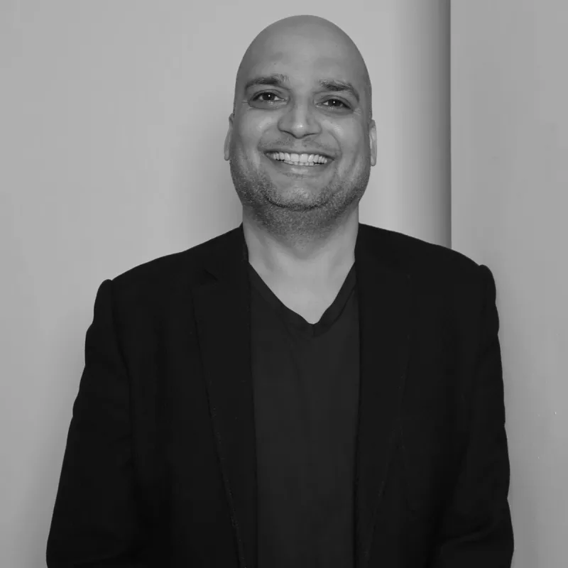 Amit J, Wholesale Manager. Professional black and white headshot, smiling in a dark shirt and blazer.
