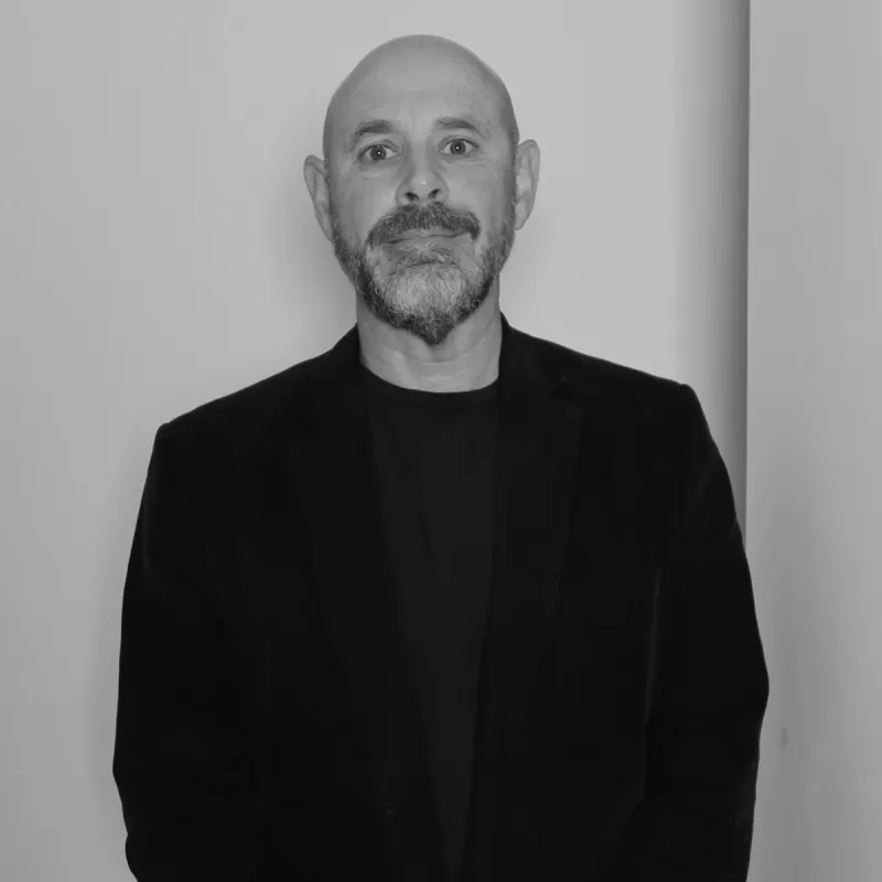 Marco D, Customer Experience Manager. Professional black and white headshot, with a beard, wearing a dark shirt.