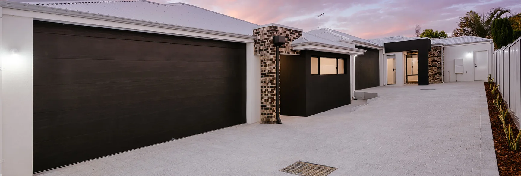 Modern house exterior with a sleek black garage door and brick accents under a pink sunset sky.