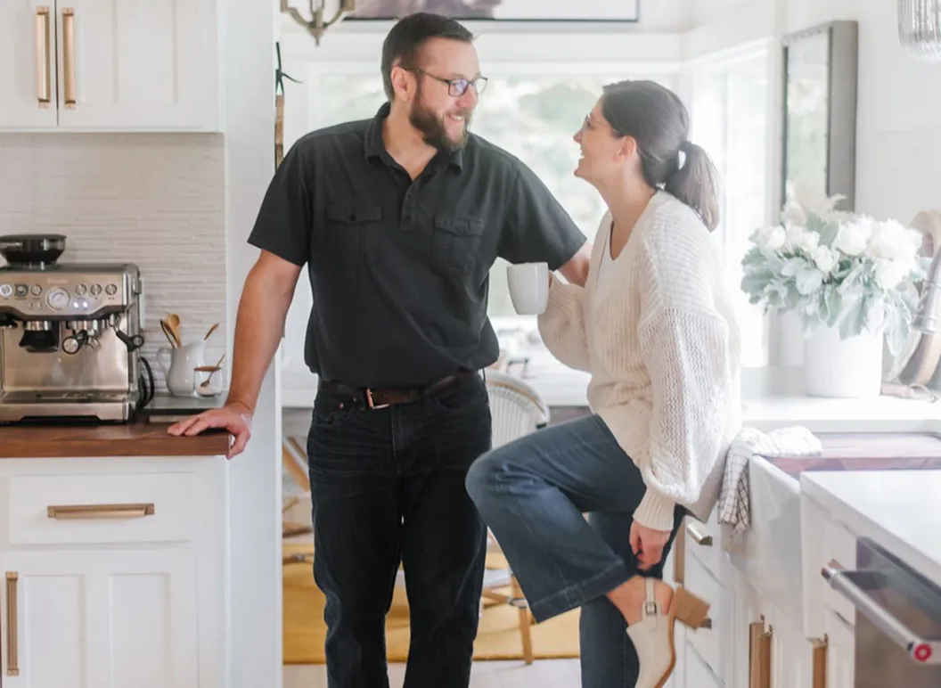Couple chatting in bright kitchen with coffee mug and espresso machine.