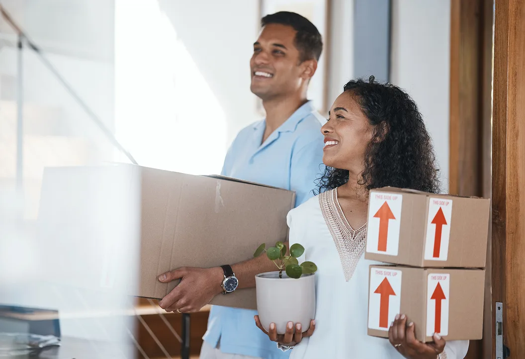 Happy couple moving into their finished Select Living home, carrying boxes and a plant during the handover stage.