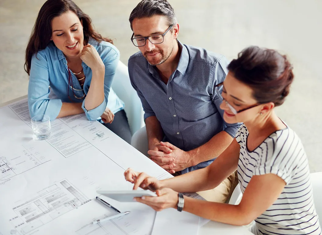 Three professionals collaborating on architectural plans at a desk.
