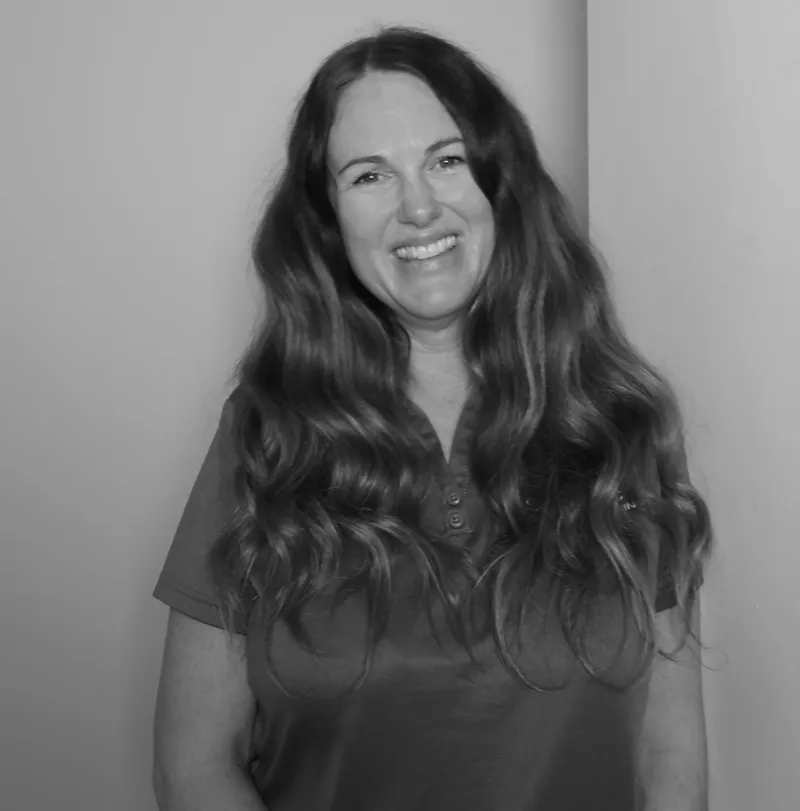 Sally S, Site Manager. Professional black and white headshot, smiling with long hair, in a branded polo shirt.